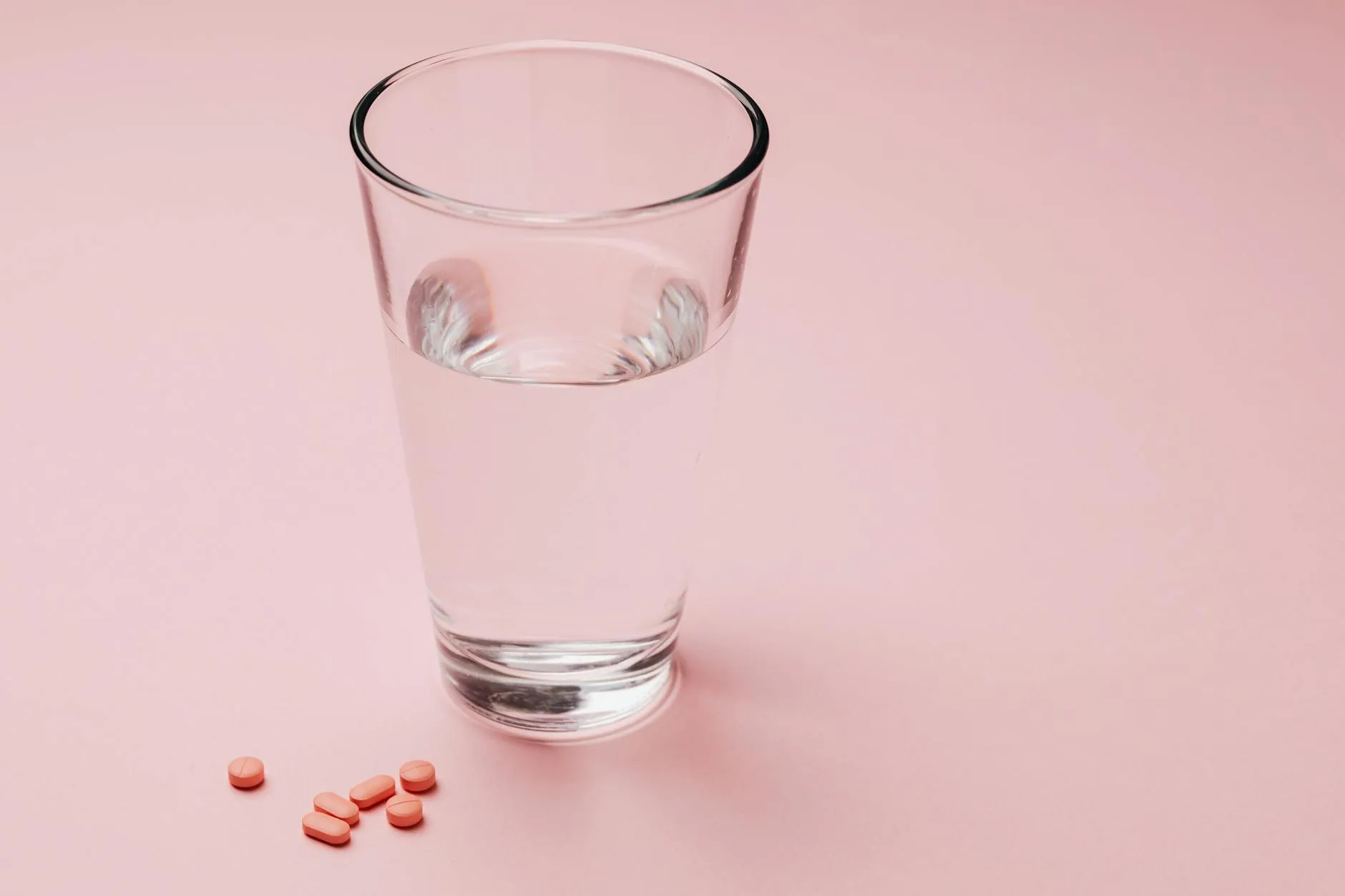 A row of supplement bottles next to a glass of water