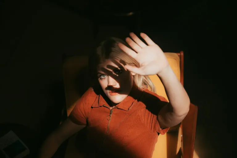 A woman in a red shirt shielding her eyes from bright light