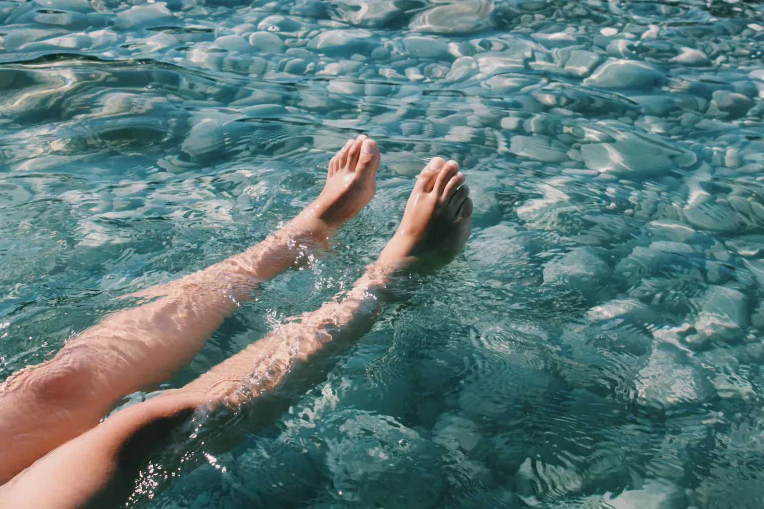 A person's legs floating in clear, sunlit water.