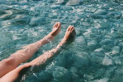 A person's legs floating in clear, sunlit water.