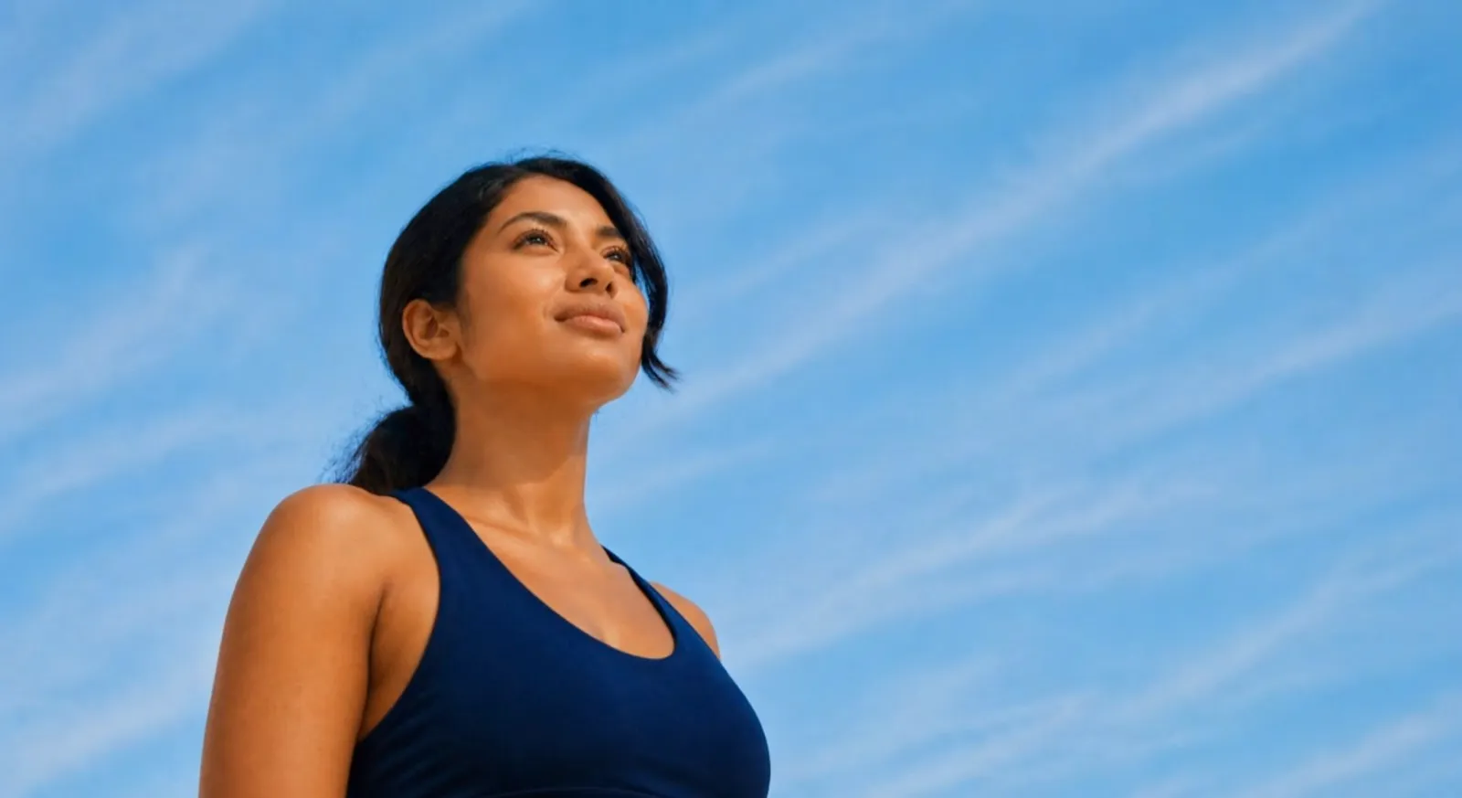 South Asian woman in a navy tank top looking up at a clear blue sky