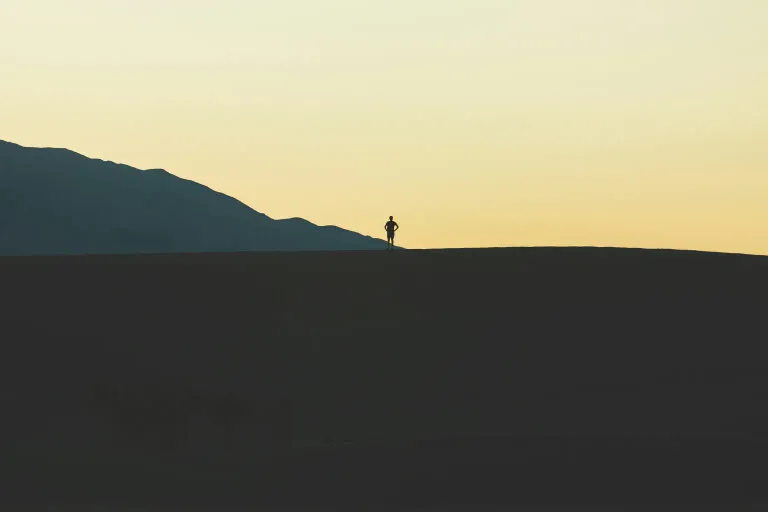 Silhouette of a hiker standing on a desert ridge at dusk