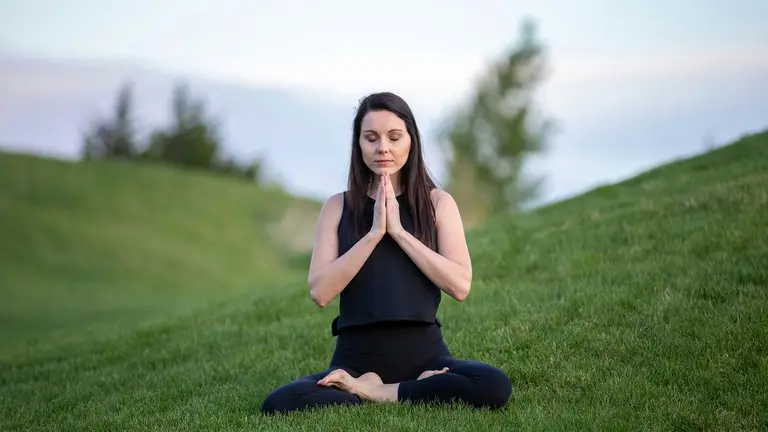 A woman practicing mindfulness meditation on a grassy hill to help manage perimenopause symptoms by balancing estrogen and progesterone levels.
