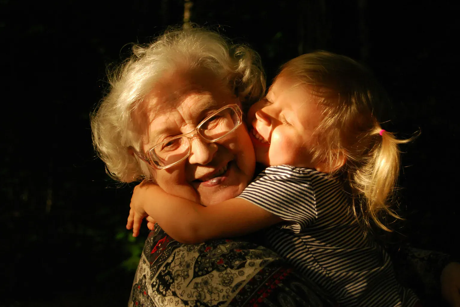 An older woman with white hair and glasses hugging a young child