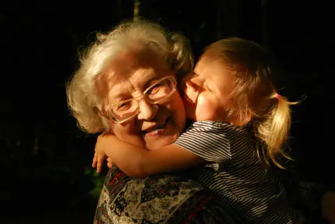 An older woman with white hair and glasses hugging a young child