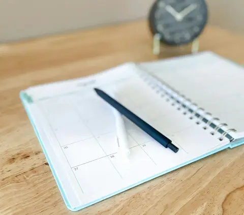 An open planner with a pen resting on a wooden desk.