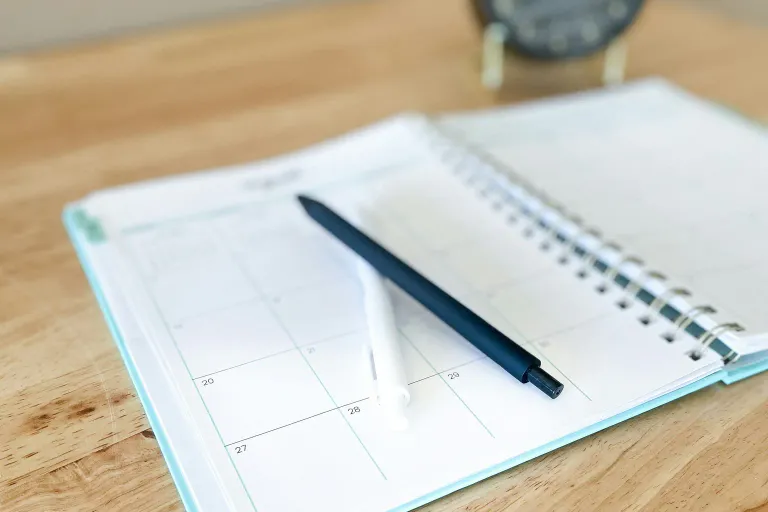 An open planner with a pen resting on a wooden desk.