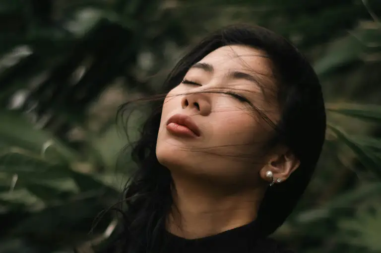A woman standing outdoors with her face turned toward the sun