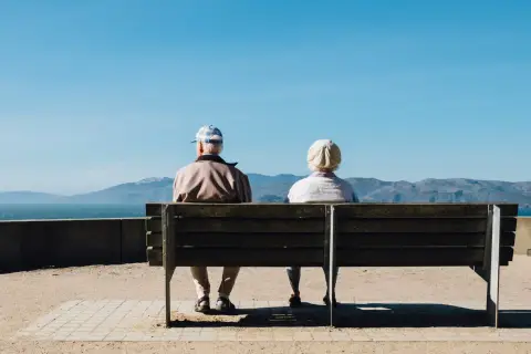 An older couple sitting together on a bench beside the sea.