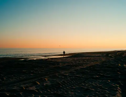 A person standing alone on a shoreline in low golden-hour light