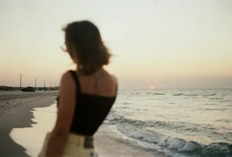 A woman walking beside the sea at sunset