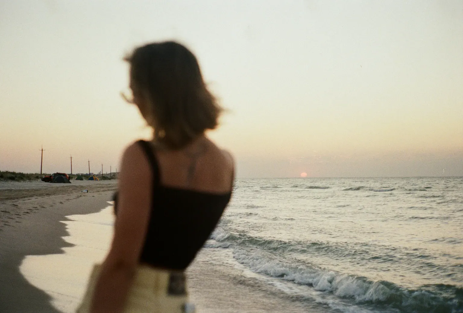 A woman standing still on a beach at golden hour, looking out at the water