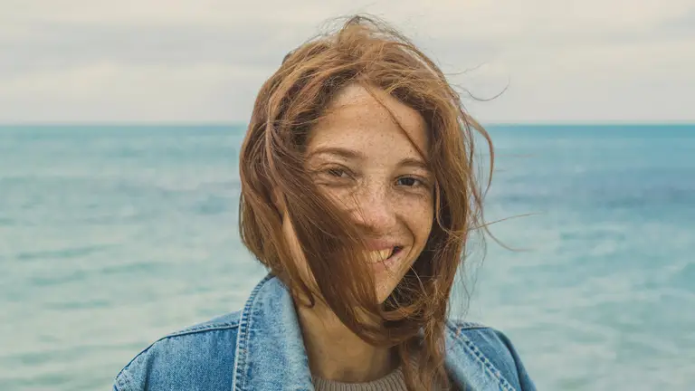 A smiling woman near the ocean, symbolizing relief from perimenopause symptoms through balanced estradiol and progesterone levels.