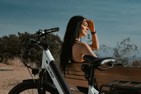 A woman sitting on a bench beside her bicycle, shading her eyes as she looks out.