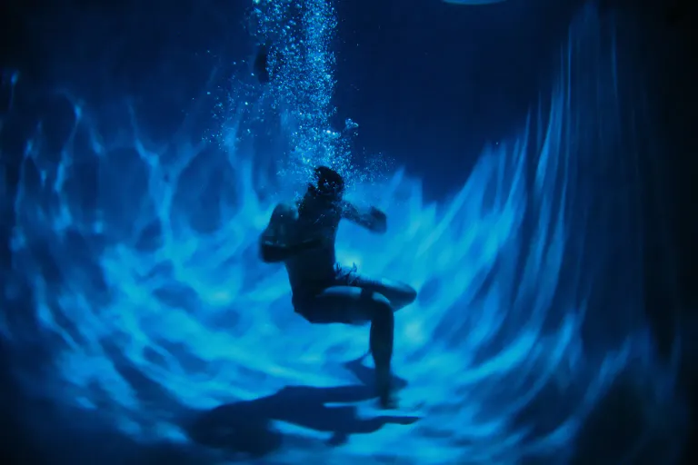 A swimmer underwater in a pool lit in deep blue