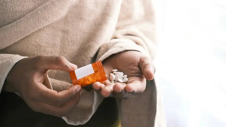 A person holding a bottle of hormone therapy pills, commonly used to balance estrogen and progesterone levels during perimenopause or postmenopause.
