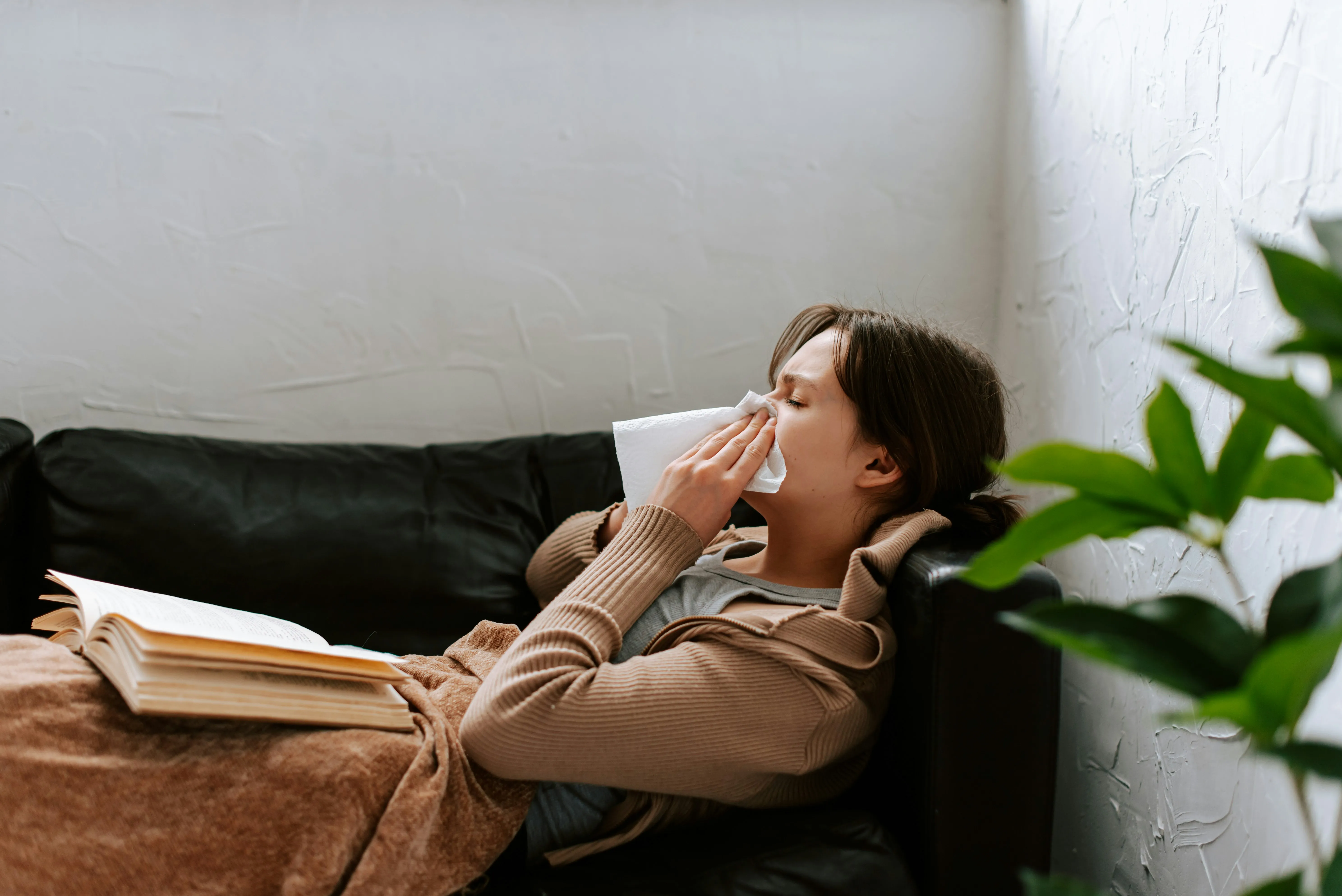 Person lying on a couch at home and blowing their nose