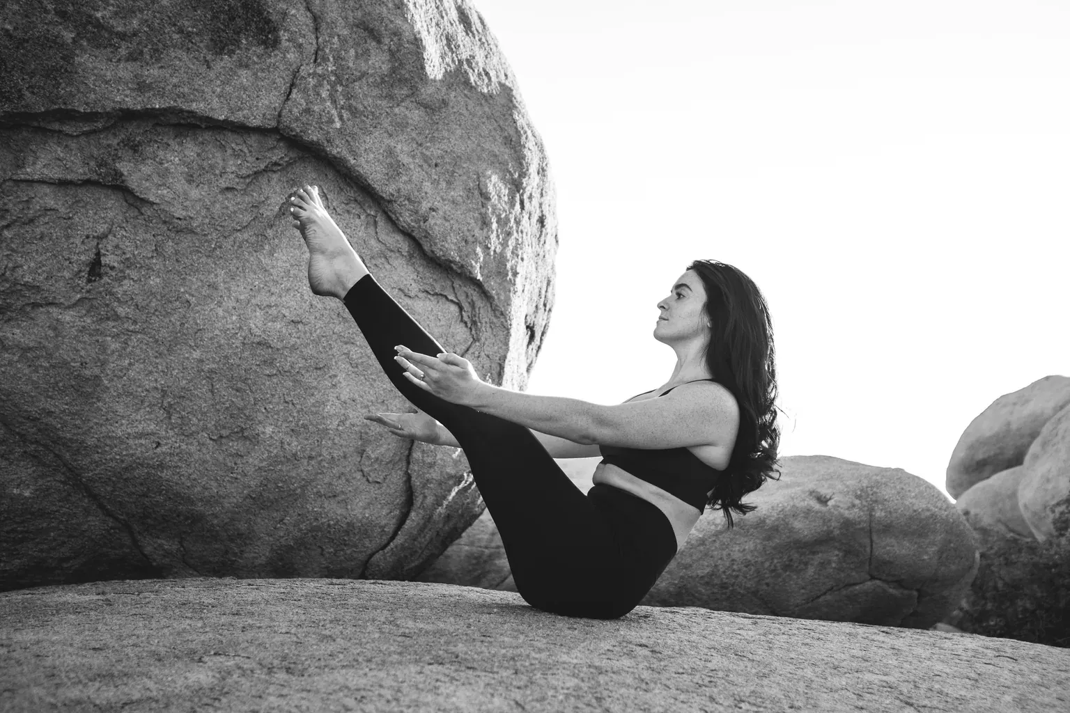 A black and white photo of a woman holding a core exercise on a large rock