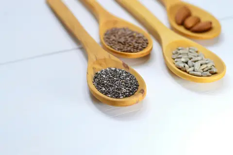 Variety of seeds and nuts in wooden spoons representing dietary vitamin E sources