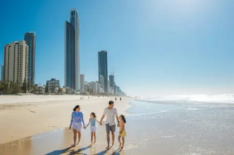 A family walking along a sunny beach with a city skyline behind them