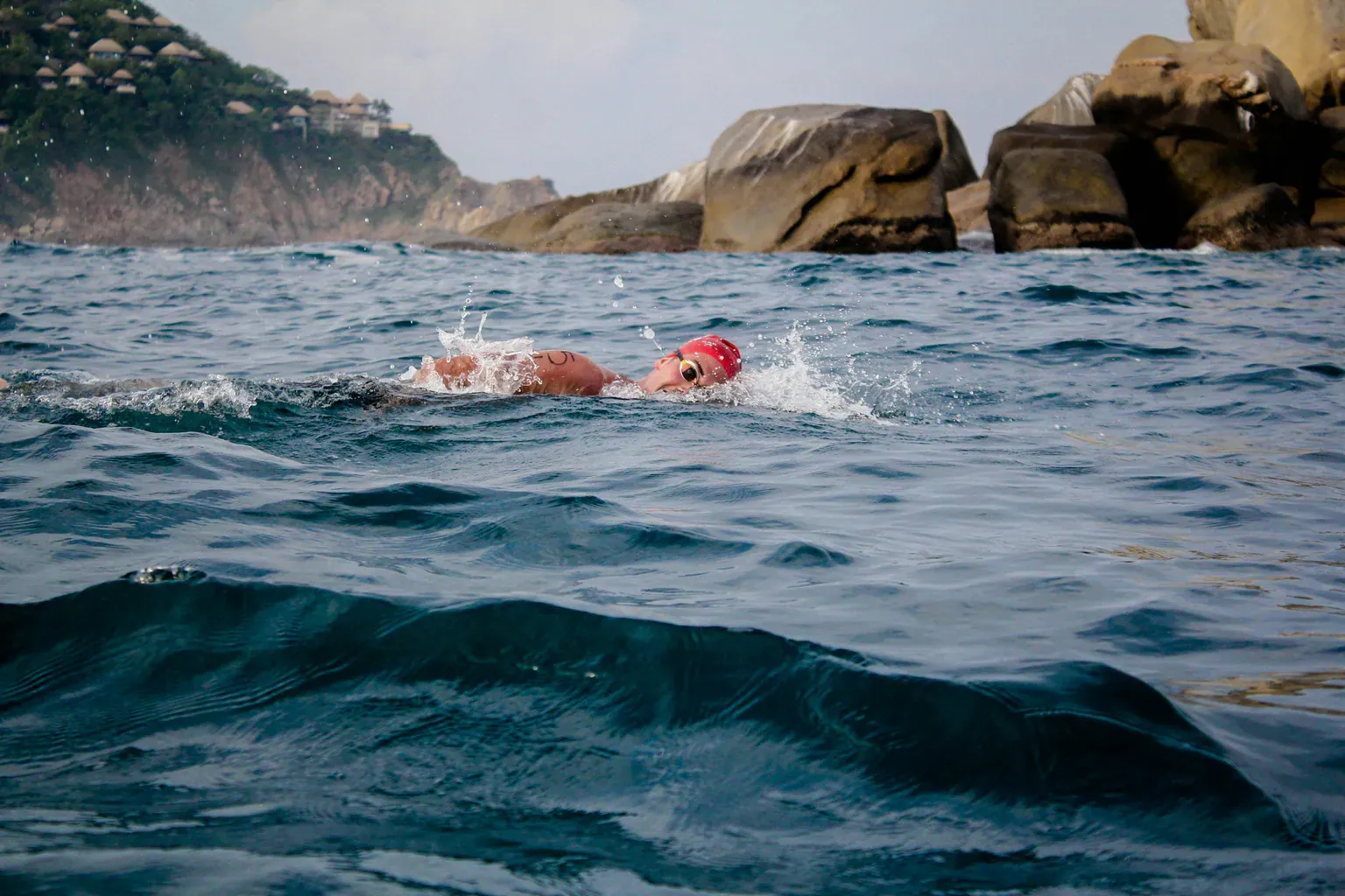 A swimmer in a red cap doing laps in open sea water