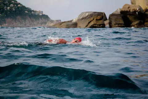 A swimmer in a red cap doing laps in open sea water